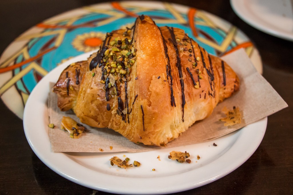 Flaky croissant drizzled with chocolate and sprinkled with chopped pistachios