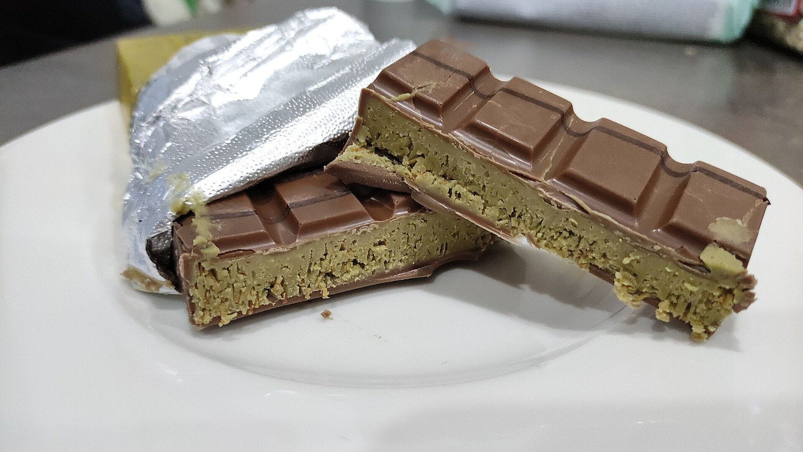 Thick chocolate bar cut open to show a green pistachio and kataifi filling on a plate