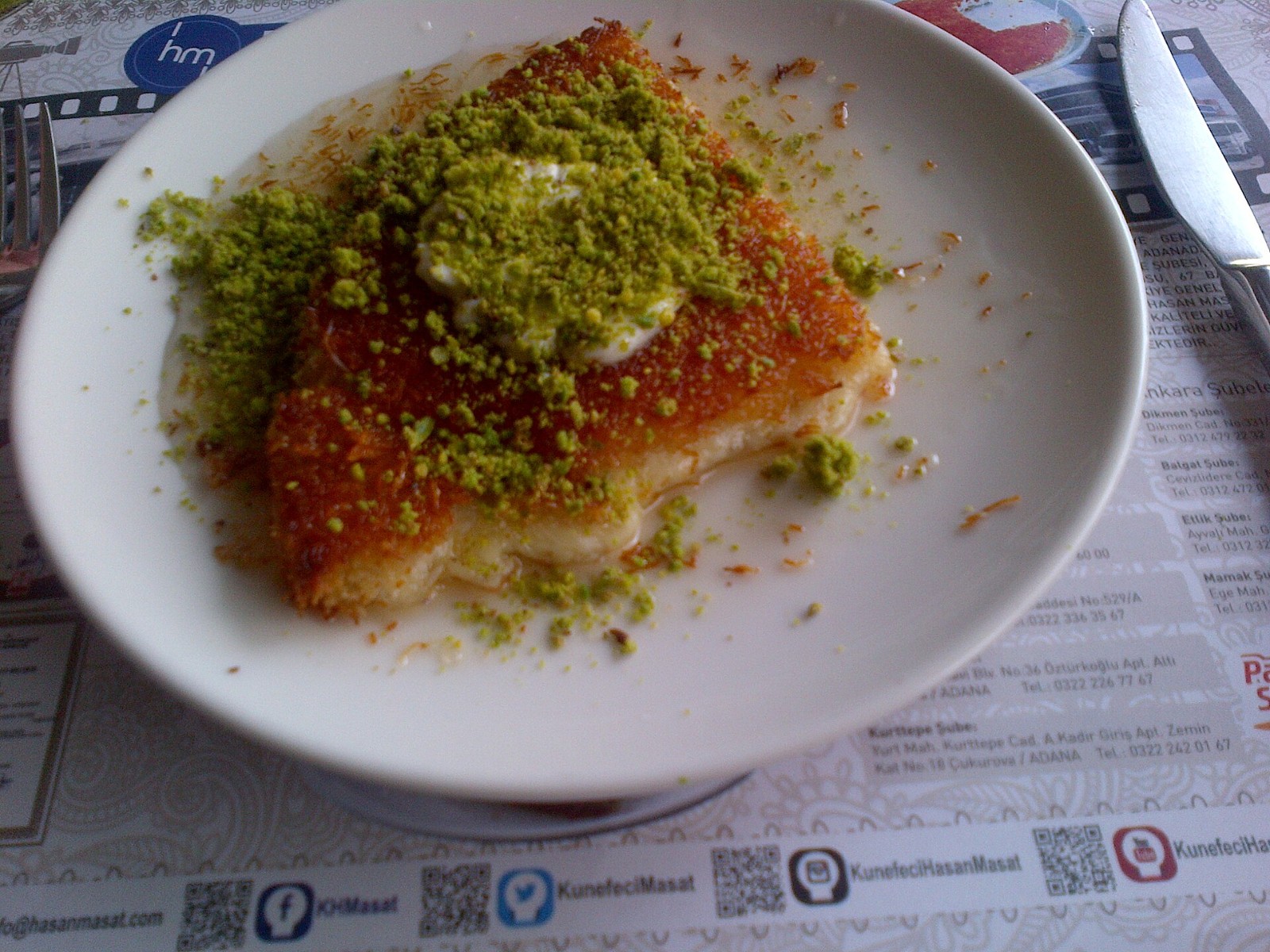 Round golden knafeh topped with crushed pistachios on a white plate