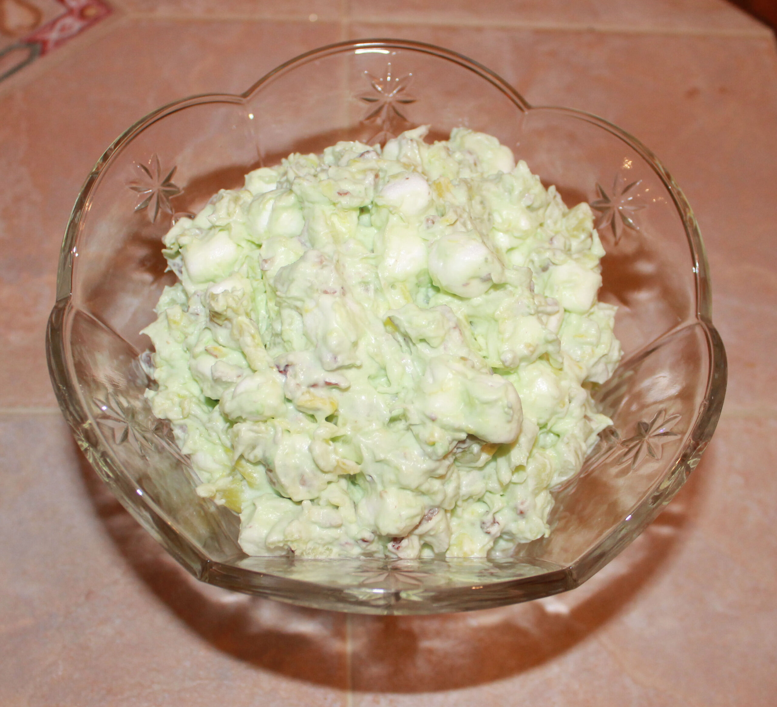 Green pistachio fluff with marshmallows and pecans in a cut glass bowl
