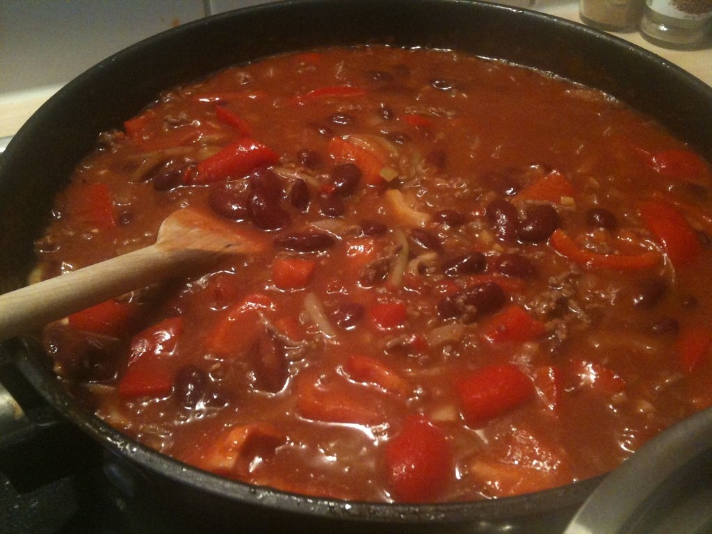 Big pot of beef and bean chili simmering with a wooden spoon