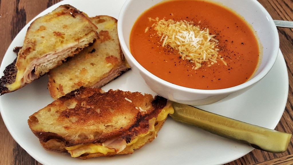 Bowl of creamy tomato soup with grilled cheese sandwich halves for dunking