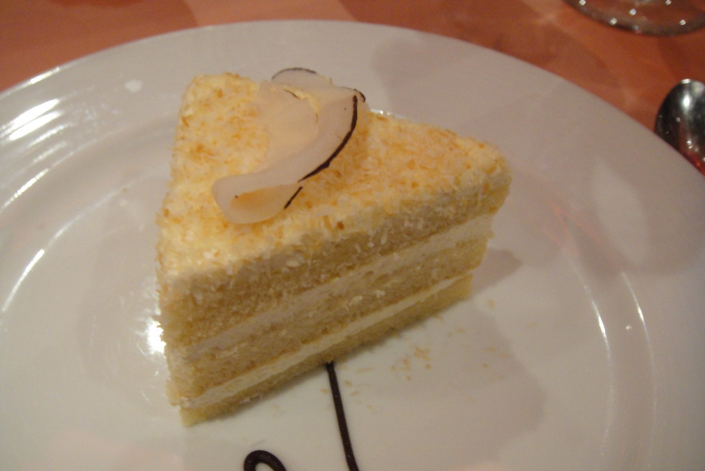 Slice of layered coconut cake with cream cheese frosting and a coconut curl