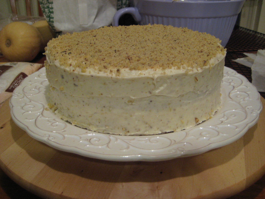 Italian cream cake with cream cheese frosting and chopped pecans on a white stand
