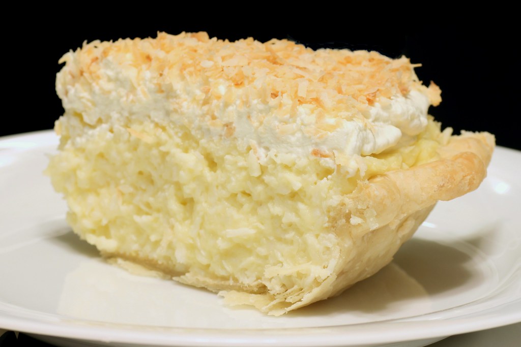 Slice of cream pie with whipped cream and toasted flakes on a white plate