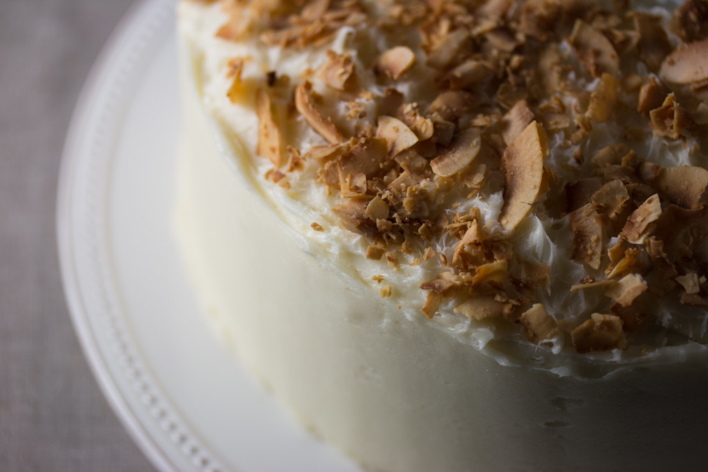 Coconut cake covered in golden toasted coconut flakes on a white cake stand