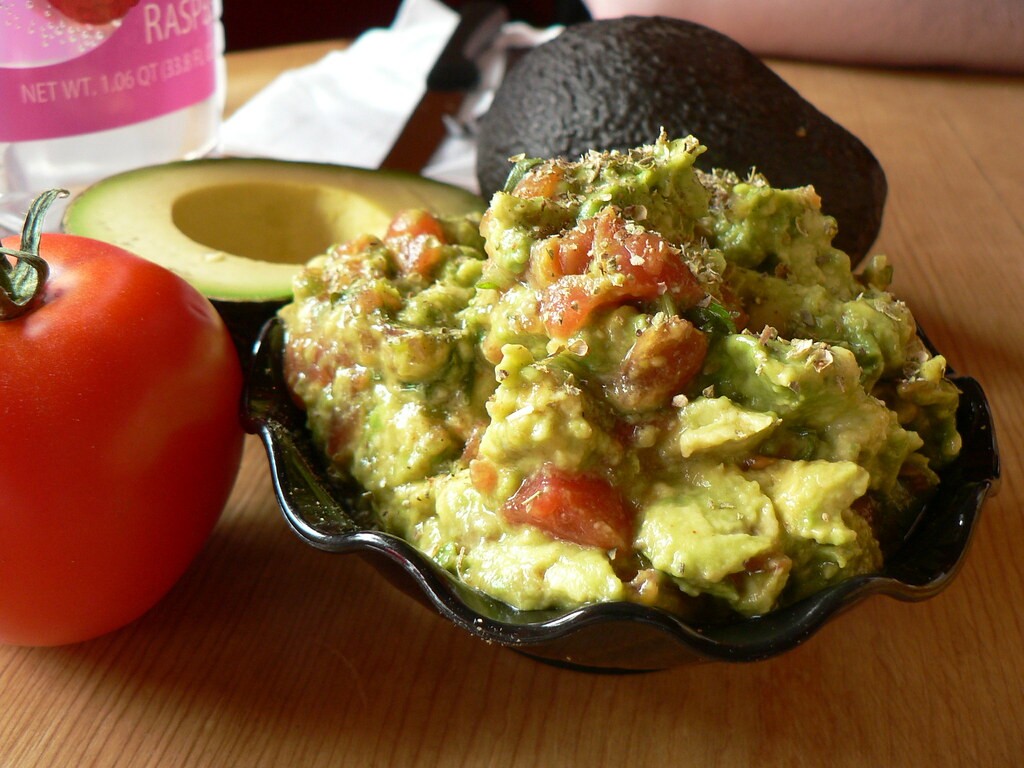 Chunky guacamole with tomato in a black bowl with fresh tomatoes