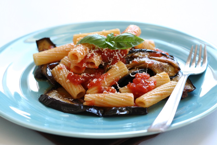Pasta alla norma with fried eggplant, tomato sauce and basil on a blue plate
