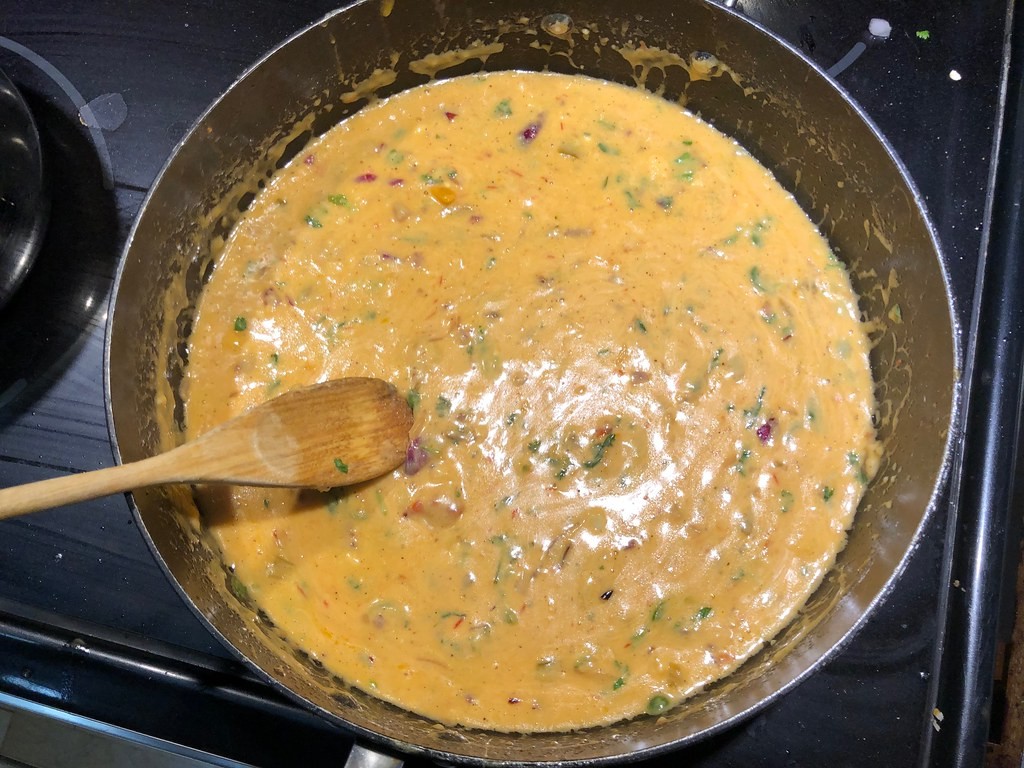 Creamy chile con queso cooking in a skillet with a wooden spoon