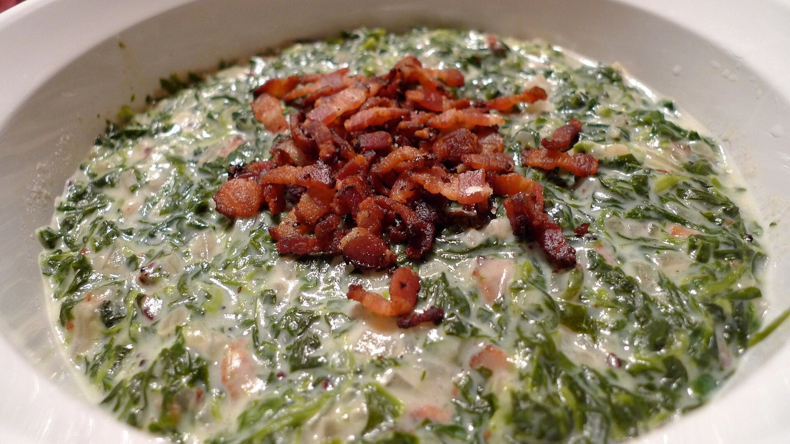 Creamed spinach topped with crispy bacon pieces in a serving dish