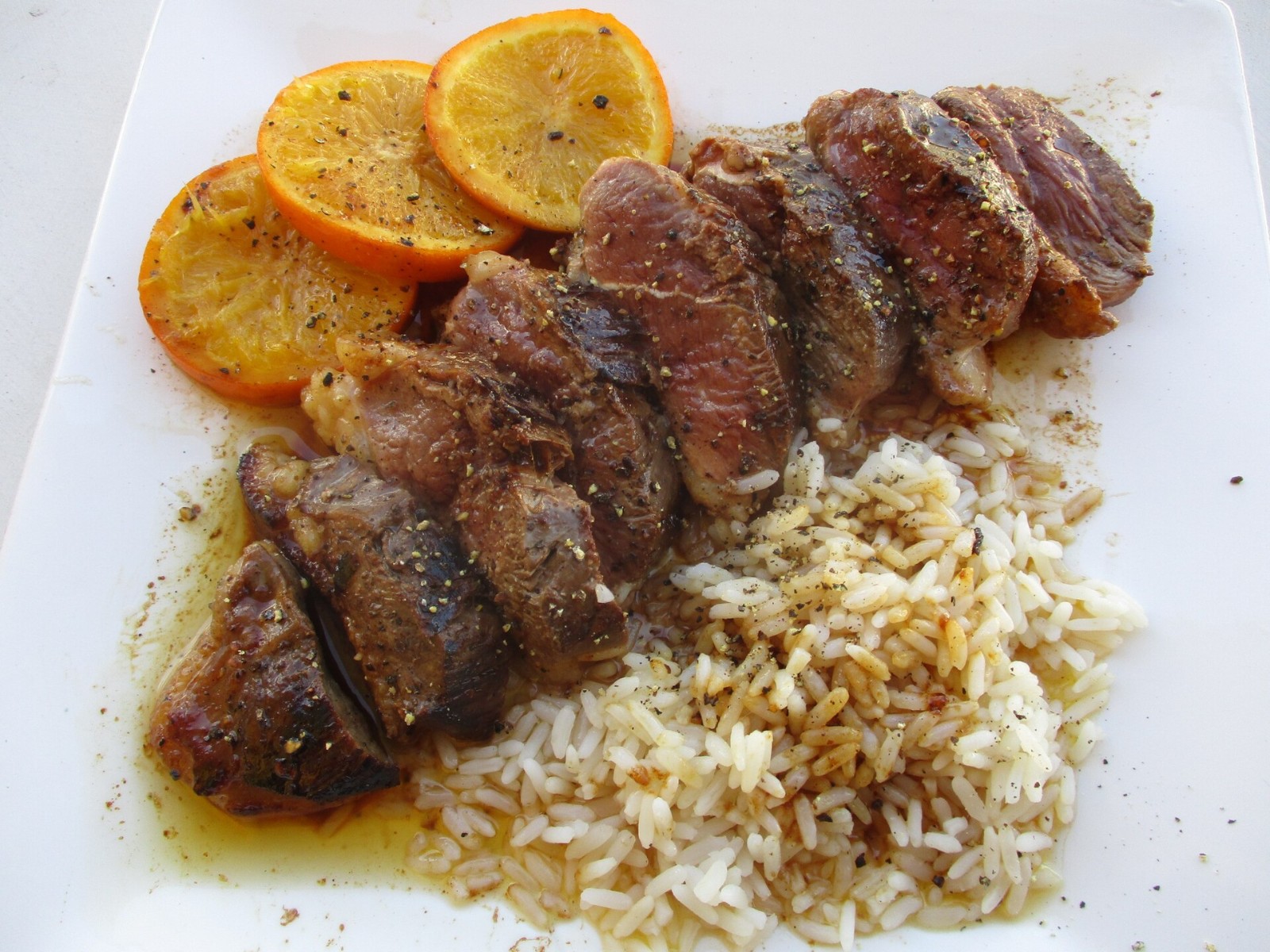 Sliced duck breast with orange sauce and orange slices on a plate