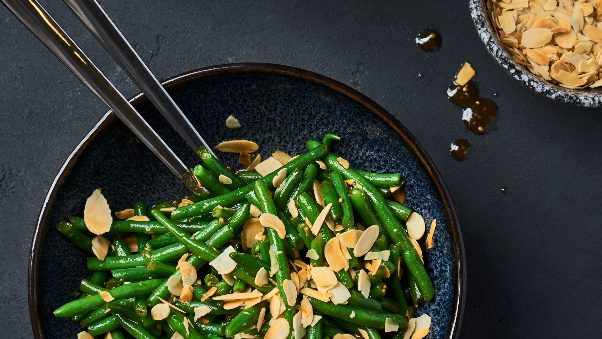 Green beans with toasted sliced almonds in a dark bowl