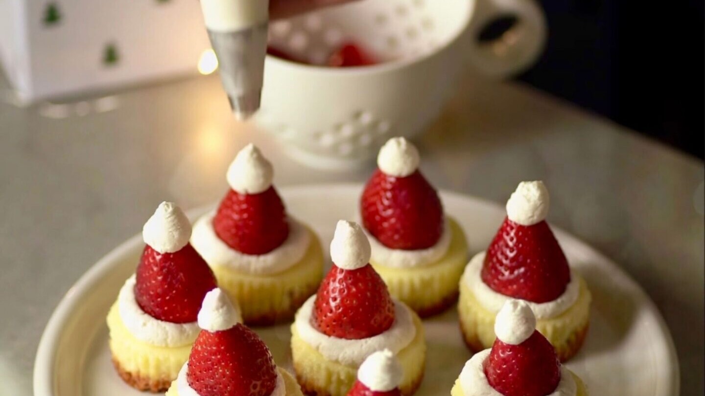 Mini cheesecakes topped with strawberries and cream like Santa hats
