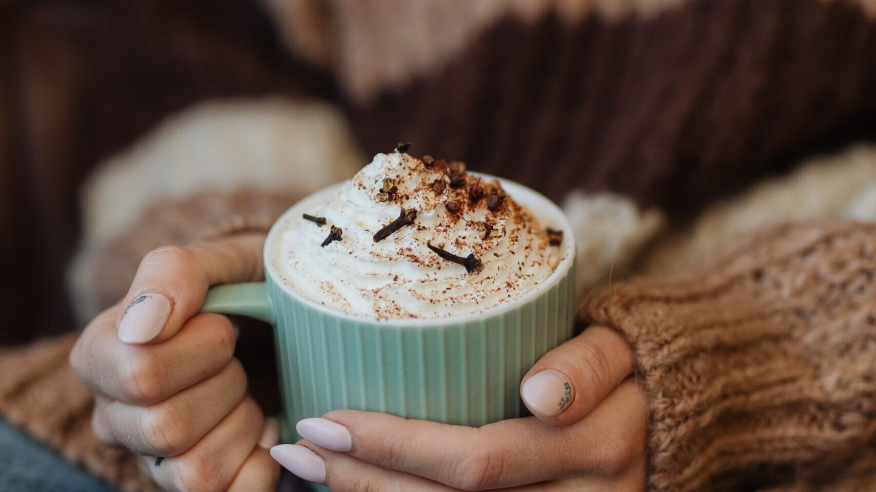 Hands holding a mug of hot cocoa topped with whipped cream