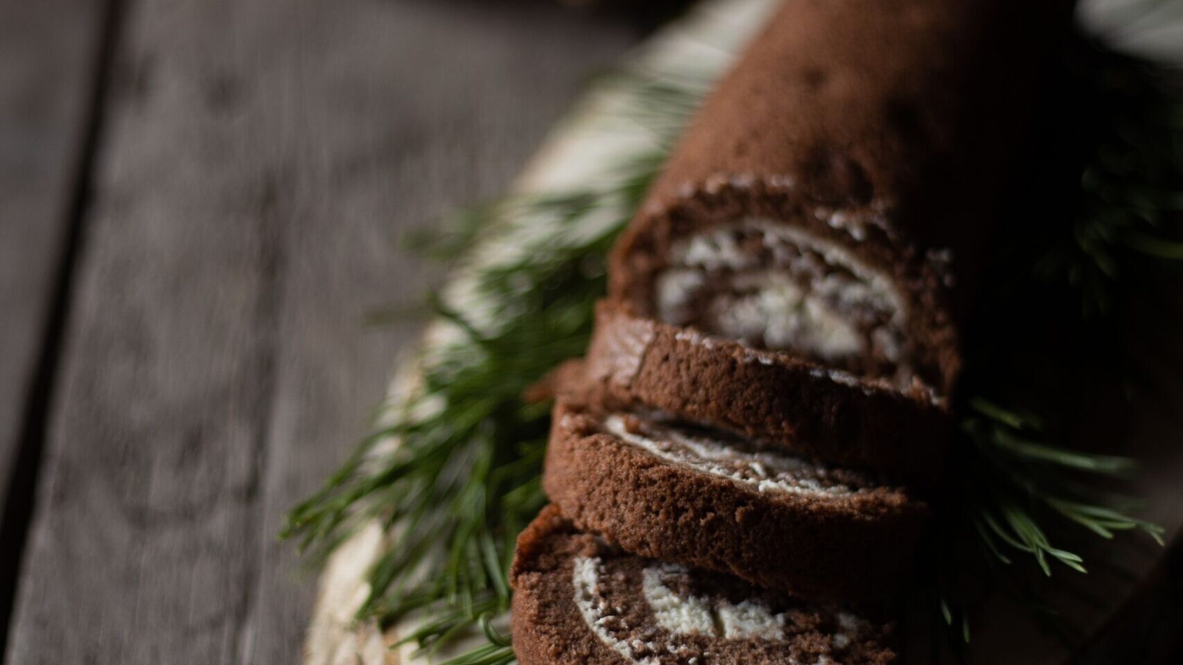 Sliced chocolate yule log roll on a wooden board with pine