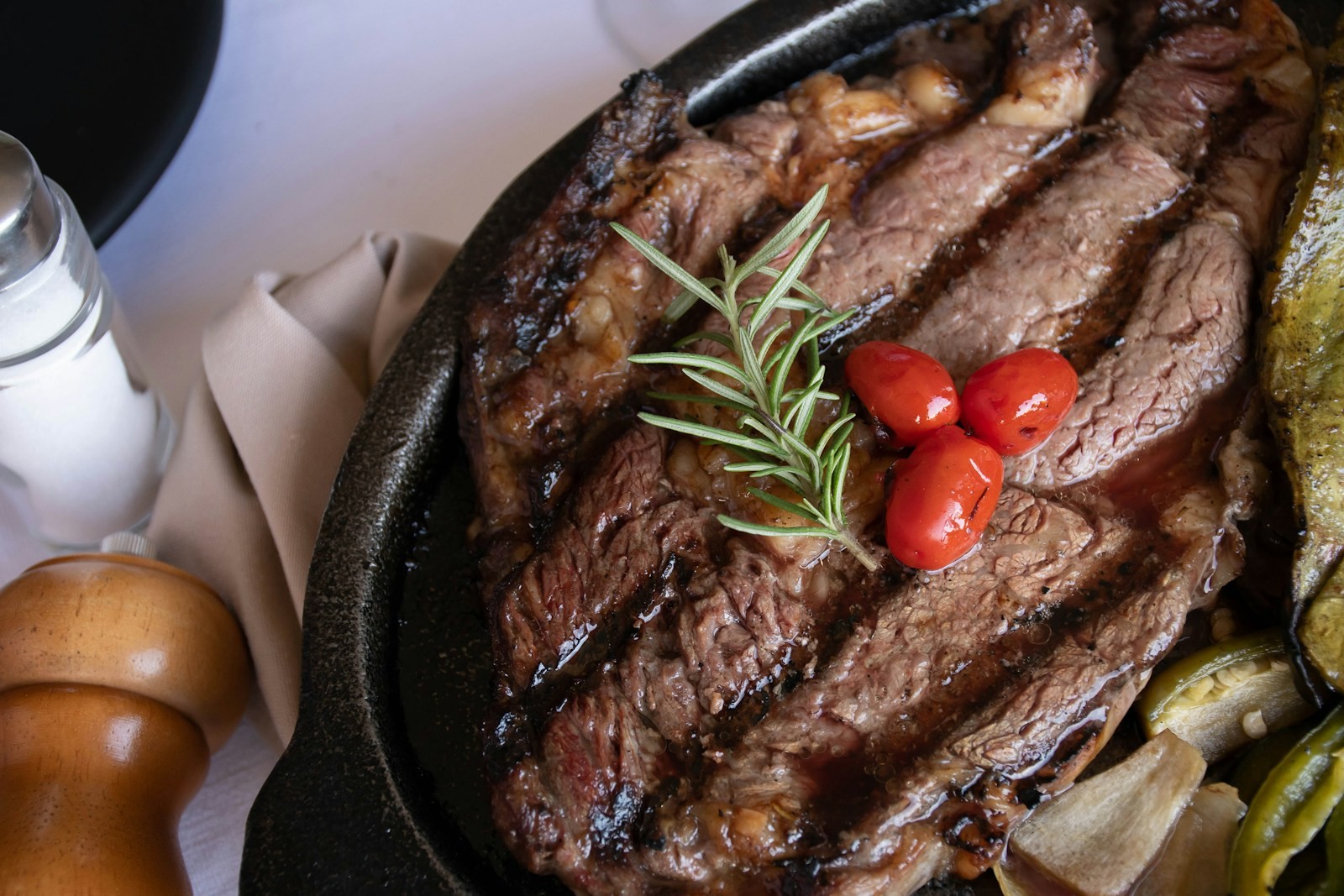 Sliced seared steak with tomatoes and greens in a black pan