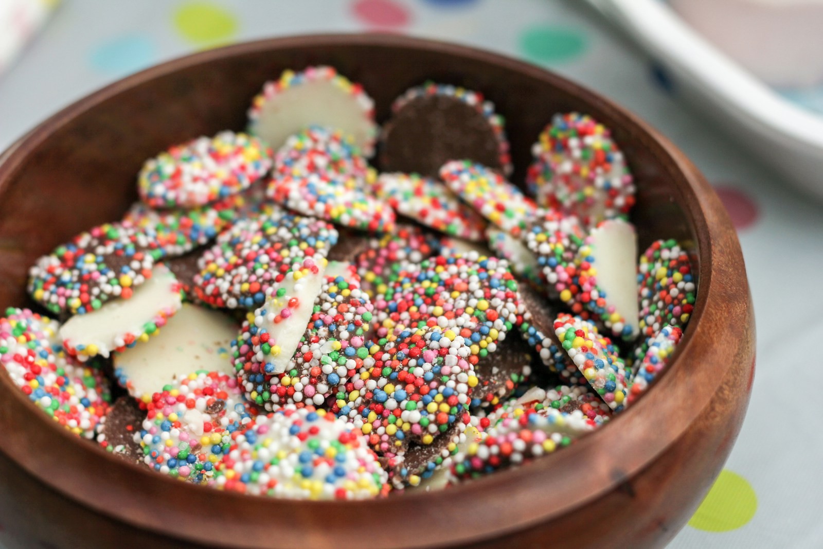 Chocolate drops covered in rainbow nonpareils in a wooden bowl