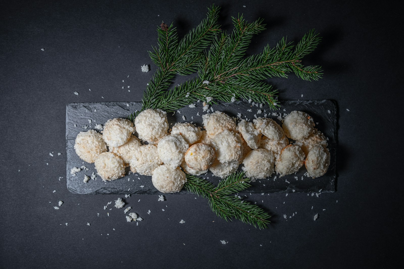 Powdered sugar snowball bites on a slate board with pine