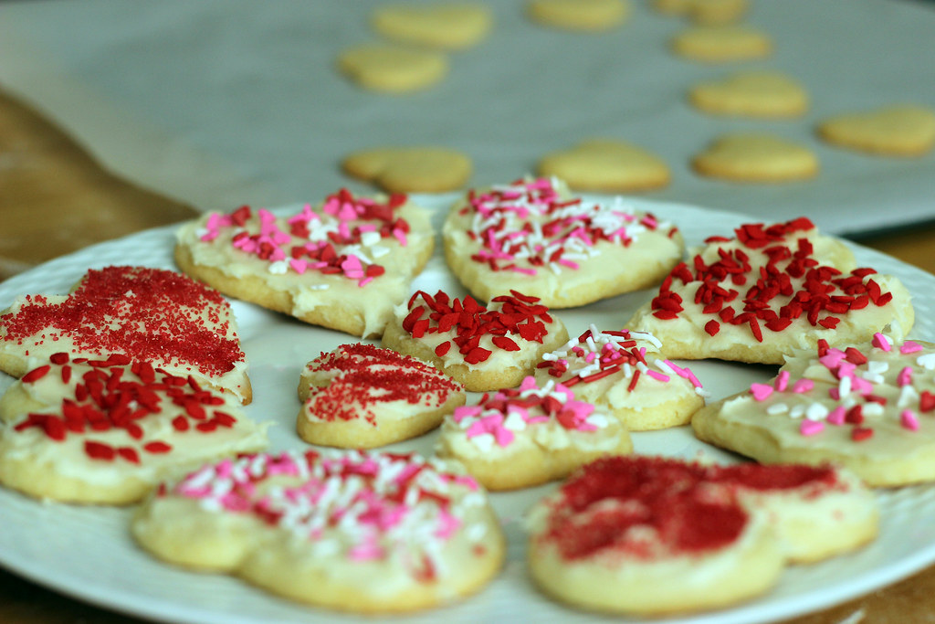 Heart cookies with white glaze, red sugar and colorful sprinkles on a pale blue plate