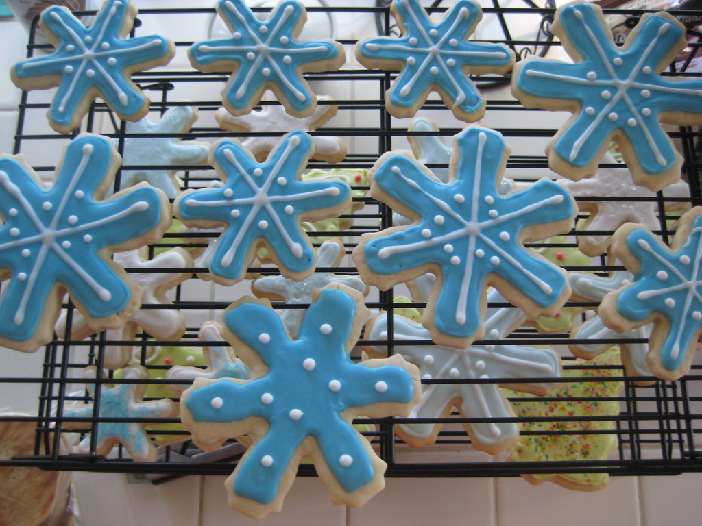 Snowflake cookies with blue icing, white piped lines and dots on a wire rack