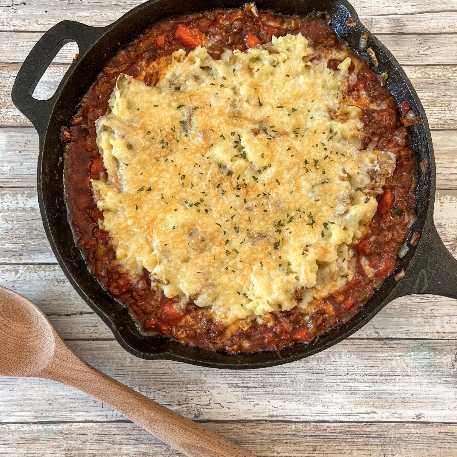 Skillet shepherd's pie with golden mashed potato topping and a wooden spoon