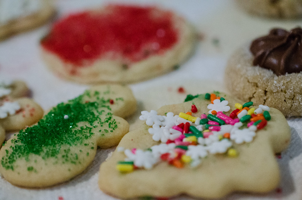 Cut-out cookies topped with green sanding sugar, red frosting and white snowflake sprinkles